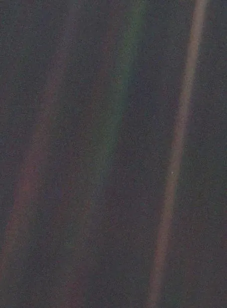 A grainy image of space with Earth appearing as a single faint point of light in a band of scattered sunlight.