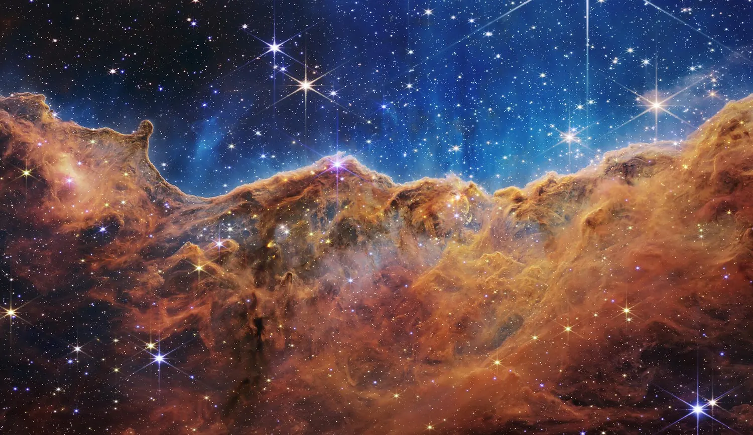 The Cosmic Cliffs in the Carina Nebula, a glowing ridge of gas studded with newborn stars.